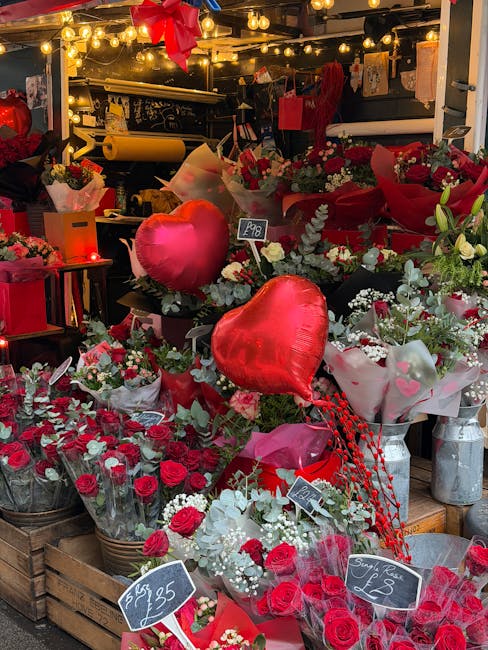 A vibrant display of fresh flowers at a florist's stall, including red roses, white baby's breath, and greenery, arranged in bouquets and wrapped in red and pink paper. Prominent among the arrangement